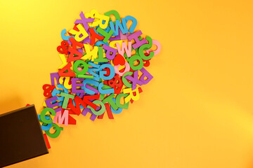 Fototapeta premium Colorful block letters flowing out from the wooden box on the yellow background 