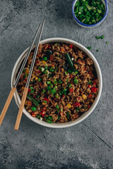 Fried Rice with vegetables, green onion and sesame in white bowl on stone background. Top view