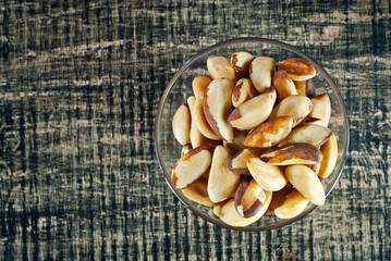Brazil nuts in a glass bowl on a wooden table. Nuts on a black shabby board. Copy space and free...