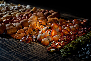 Many kinds of nuts close up. Heap of nuts on a black wooden board. Nuts are stacked on the table. Contrasting dramatic light as an artistic effect.