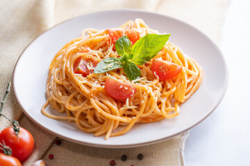 Tasty appetizing classic italian spaghetti pasta with tomato sauce, cheese parmesan and basil on plate and ingredients for cooking pasta on white marble table.