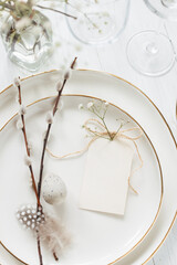 Easter table setting with willow twigs, quail eggs and tag. Golden cutlery and golden rim plates. Close up view.