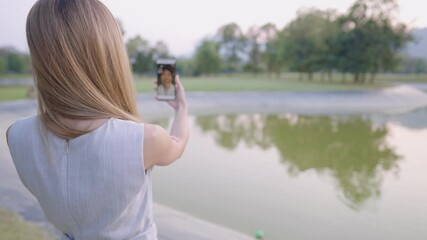 Young attractive blonde lady doing video call while standing outside from home in green park, missing love one friend family, happy moment, smiling cheerfully, homesick concepts, on travelling, 