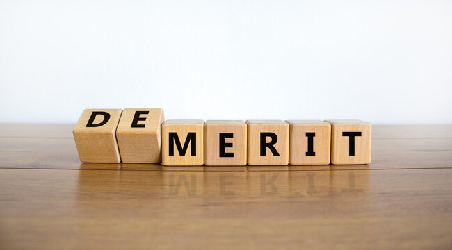 Demerit or merit symbol. Turned wooden cubes and changed words 'demerit' to 'merit'. Beautiful wooden table, white background, copy space. Business and demerit or merit concept.