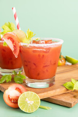glass glass of tomato juice, lime with fresh bright bunch of tomatoes isolated on green background, green parsley. vegetable drink.