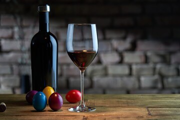 Easter decorations, colorful eggs, a glass of red wine with a bottle on table at home dark warm living room, brick wall in background. Copy space for text.