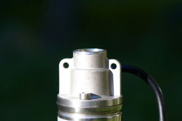 Top of the pump with black cable on a dark green background. Borehole pump outlet thread. The top...