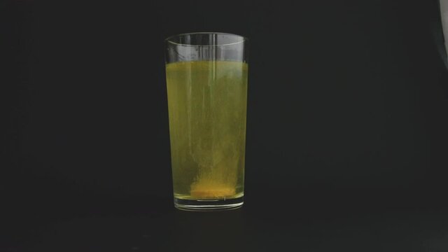 A tablet of vitamin C falls into a glass beaker with water. The tablet is water-soluble. When dissolved, it hisses, rages.