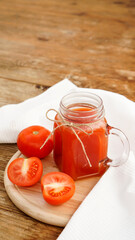 Tomato juice in glass jar and fresh tomatoes on wooden cutting board and white towel