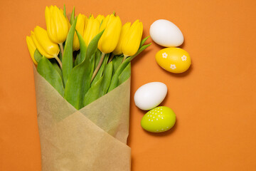 easter eggs and flowers. Colored Easter eggs next to a bouquet of tulips on an orange background. Green, yellow and white Easter eggs. Copy space. Spring mood. 