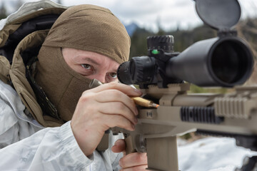 Army Man wearing Tactical Uniform with Sniper River Camouflaged in Snow Aiming at the Target. Winter Warfare. Taken in British Columbia, Canada.