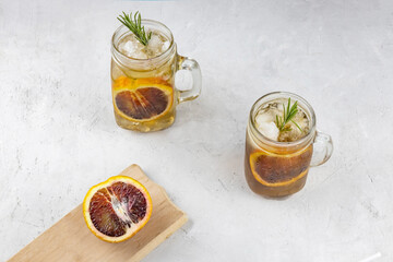 alcoholic kombucha cocktail with a slice of red orange, ice and a sprig of rosemary