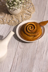 Freshly baked cinnamon bun stuffed with spices and cocoa on a white woden table with a tough shade. Sweet homemade cakes.