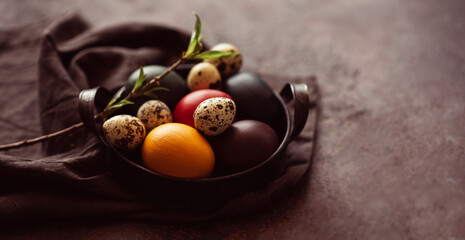 Vintage iron tray full of colorful Easter eggs with hay and spring branch on a dark rustic background. Copy space.