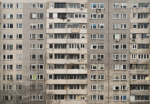 Window pattern of a facade of an old building with many flats and flats in the middle class suburbs of the city of Warsaw in Poland, grey and sad decaying building.
