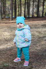 Toddler child standing alone in spring forests, wearing blue hat, jacket and trousers