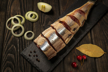 Raw Norwegian herring with onions and spices on a serving board close-up. The idea of a snack for a street cafe. Top view