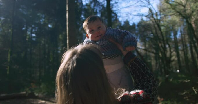 A young mother in the woods is lifting her baby up in the air on a sunny spring day
