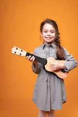Fototapeta premium Little girl in pigtails are holding a small guitar in their hands while standing on a bright background