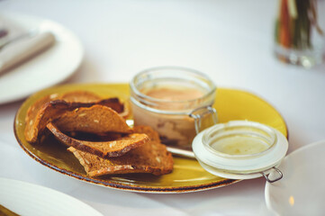 Fresh homemade chicken liver pate in a glass bowl or mold and slices of seed bread with herb and garlic pate on the table. Close-up