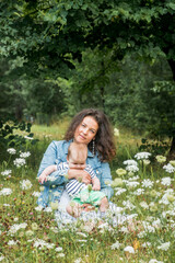 mom and baby are sitting in a park under a tree among the flowers and smiling.Flower field, picnic outdoors