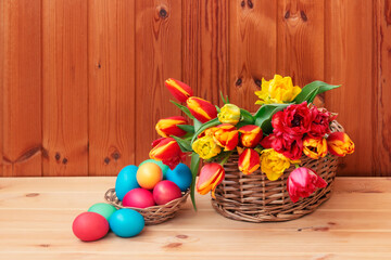 Obraz na płótnie Canvas Easter concept. Colorful tulips and Easter eggs in wicker baskets on wooden table. Selective focus.