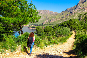 A young girl walking hiking on a path on a beautiful mediterranean forest along the coast of balearic island of Mallorca with the mountains at the background