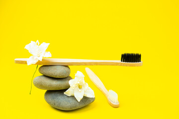 On a yellow background, bamboo toothbrushes. Equilibrium of toothbrushes on pebbles.