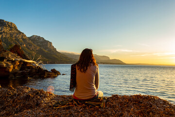 A young and beautiful girl dressed in casual clothes looking at the sunset at a beautiful beach in Artà Mallorca Balearic Islands Spain with a impressive view of the sea and the Tramuntana mountains