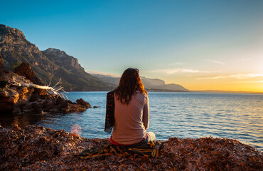 A young and beautiful girl dressed in casual clothes looking at the sunset at a beautiful beach in Artà Mallorca Balearic Islands Spain with a impressive view of the sea and the Tramuntana mountains