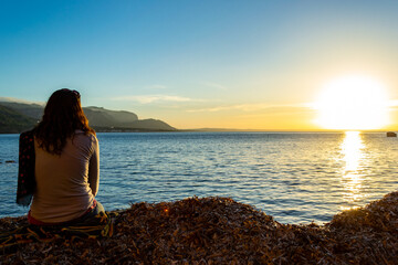 A young and beautiful girl dressed in casual clothes looking at the sunset at a beautiful beach in Artà Mallorca Balearic Islands Spain with a impressive view of the sea and the Tramuntana mountains