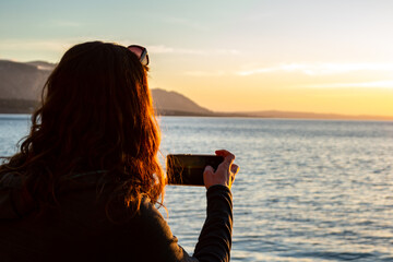 A young and beautiful girl dressed in casual clothes looking at the sunset at a beautiful beach in Artà Mallorca Balearic Islands Spain with a impressive view of the sea and the Tramuntana mountains