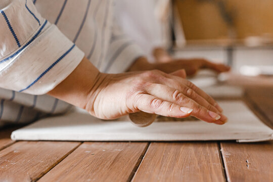 Female hands roll out the clay with a rolling pin on the table in the pottery