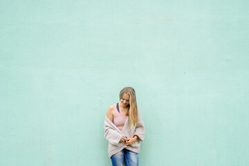 Fototapeta premium Portrait of pretty caucasian girl standing against blue city wall background. Student, online work
