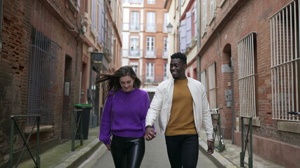 Fototapeta na wymiar Diversity concept. Interracial couple holding hands walking outside in european street
