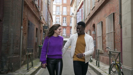 Fototapeta premium Diversity concept. Interracial couple holding hands walking outside in european street