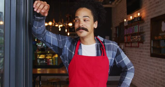 Mixed race male barista with moustache leaning in the doorway of cafe smiling