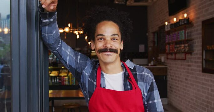 Mixed race male barista with moustache leaning in the doorway of cafe smiling