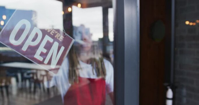 Mixed race male barista with dreadlocks closing the door and switching the sign from open to closed
