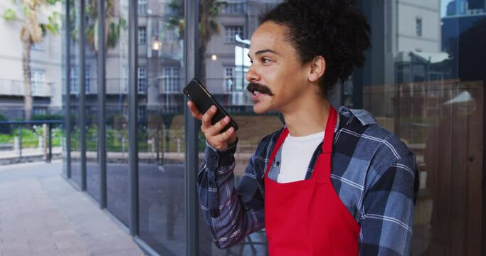 Mixed race male barista with moustache wearing an apron talking on smartphone
