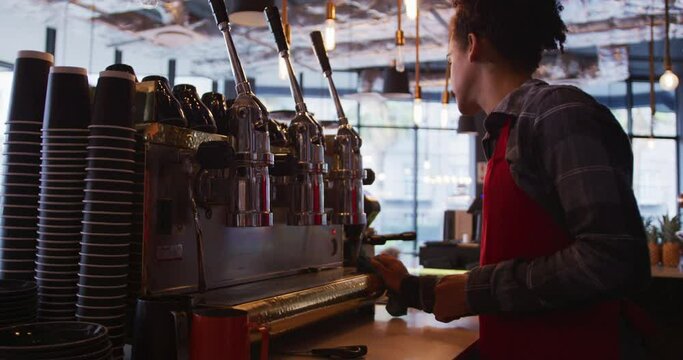 Mixed race male barista wearing an apron cleaning the cafe coffee machine and counter