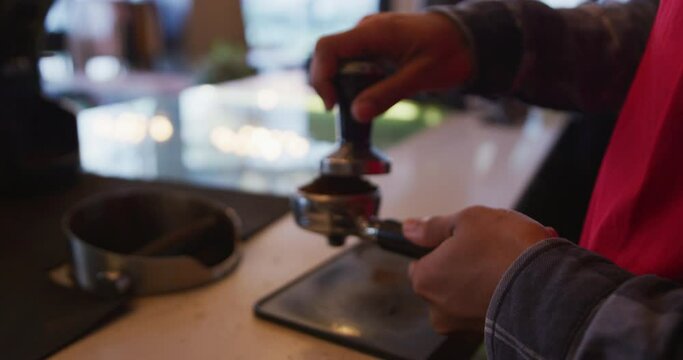 Hands of mixed race male barista wearing an apron preparing takeaway coffee