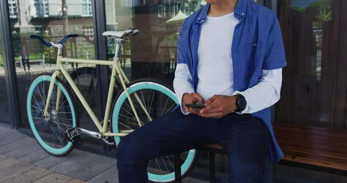 Mixed race man with moustache sitting in street using smartphone
