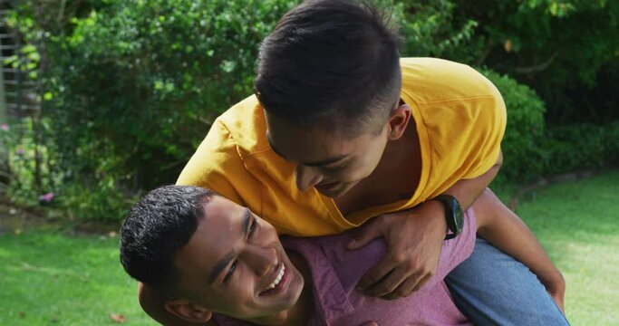Smiling mixed race gay male couple having fun piggybacking in garden