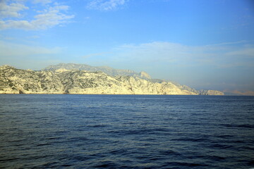 Naklejka premium Rocky outcrop on the sea with cloudy sky and coast in the background, Parc National des Calanques, Marseille, France