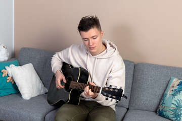 A young man sits on the couch at home and plays the guitar. High quality photo