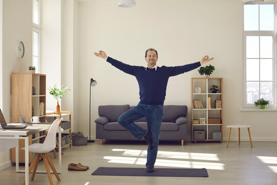 Senior man taking break from work in business office. Happy calm mature businessman doing Vrikshasana or Tree Pose with eyes closed while practising yoga exercise during working day in his workplace
