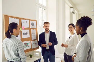 Cheerful diverse office workers discuss financial risks and analyze charts and diagrams together. Positive colleagues discuss a new business project. Concept of planning, brainstorming and teamwork.