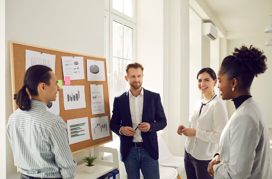 Cheerful Diverse Office Workers Discuss Financial Risks And Analyze Charts And Diagrams Together. Positive Colleagues Discuss A New Business Project. Concept Of Planning, Brainstorming And Teamwork.