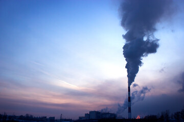 large chimney with black smoke against the background of the sunset sky on